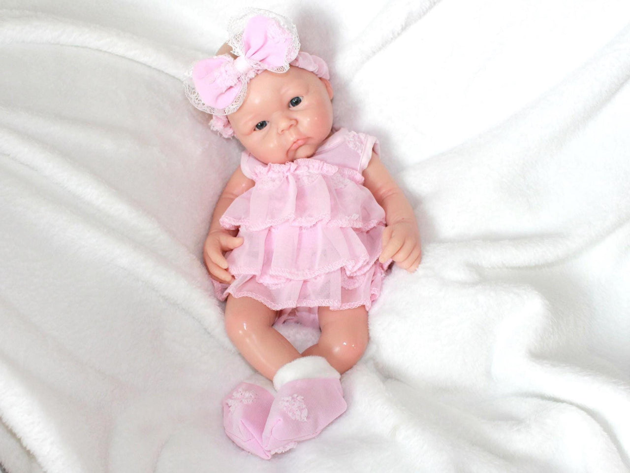 Lifelike reborn baby doll with blue eyes dressed in pink ruffle dress and matching bow headband, realistic handmade newborn doll