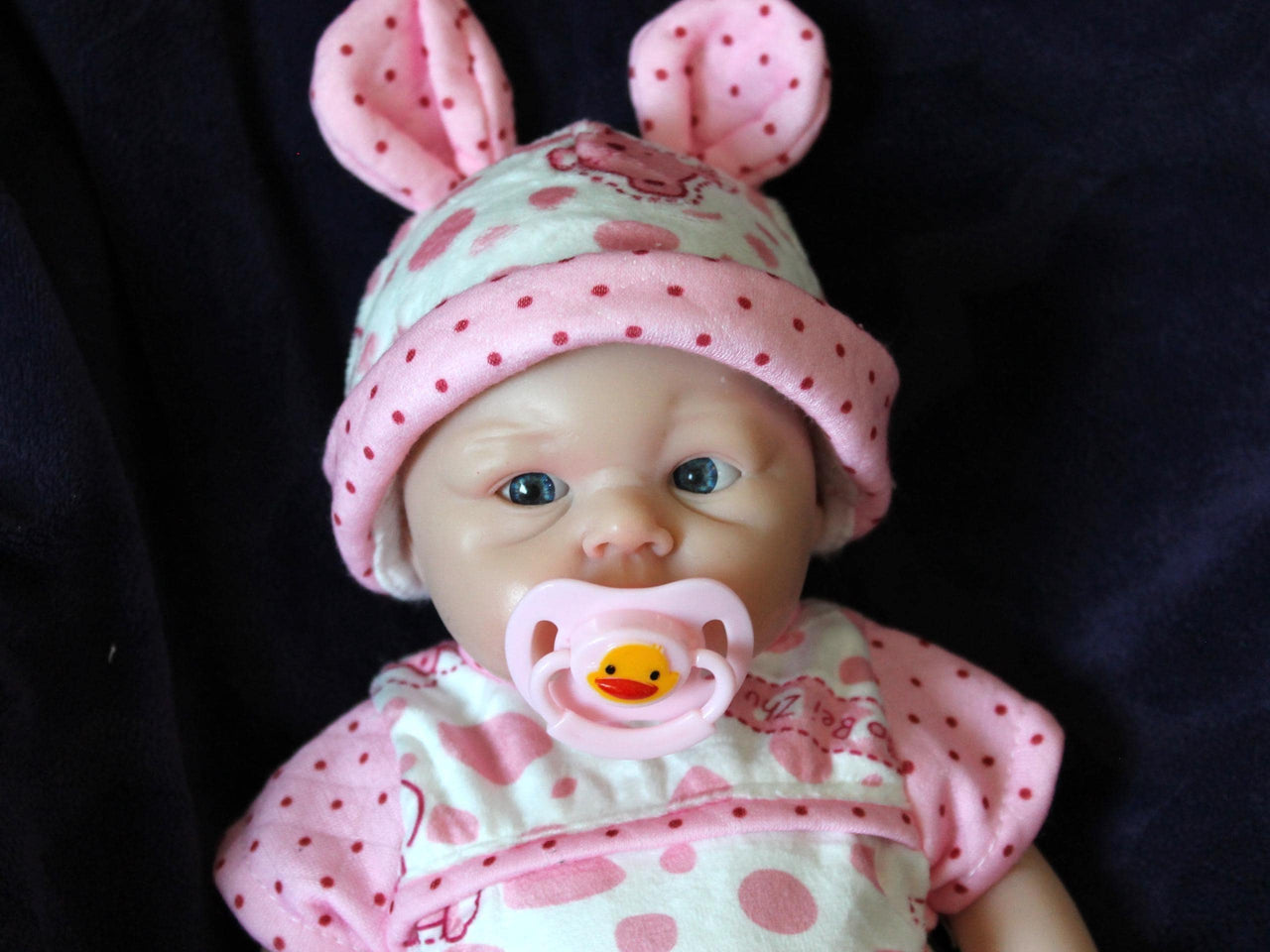 Realistic reborn baby doll dressed in pink bear-print outfit and matching hat, handmade newborn doll for collectors, play, or therapy
