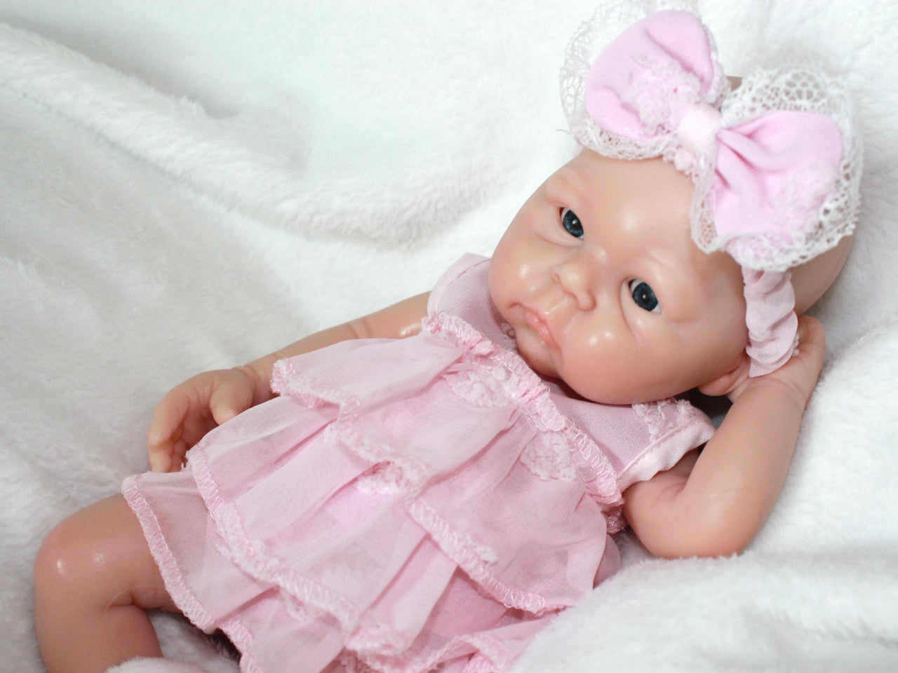 A baby doll adorned in a pink dress and headband, positioned on a light-colored surface.