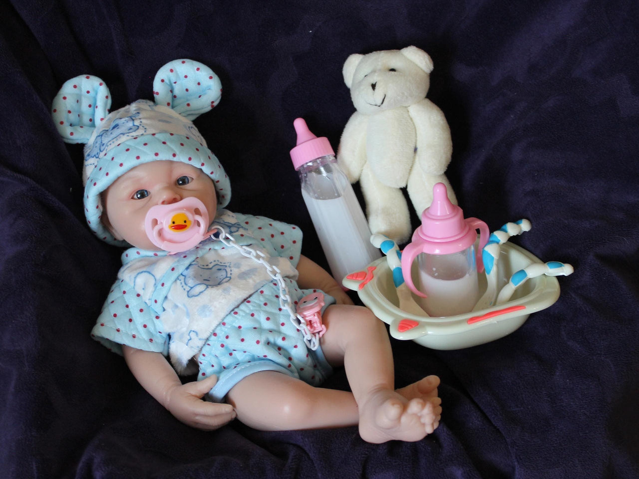 Lifelike reborn baby doll with blue eyes wearing blue bear-print outfit and matching bunny ear hat, realistic handmade newborn doll