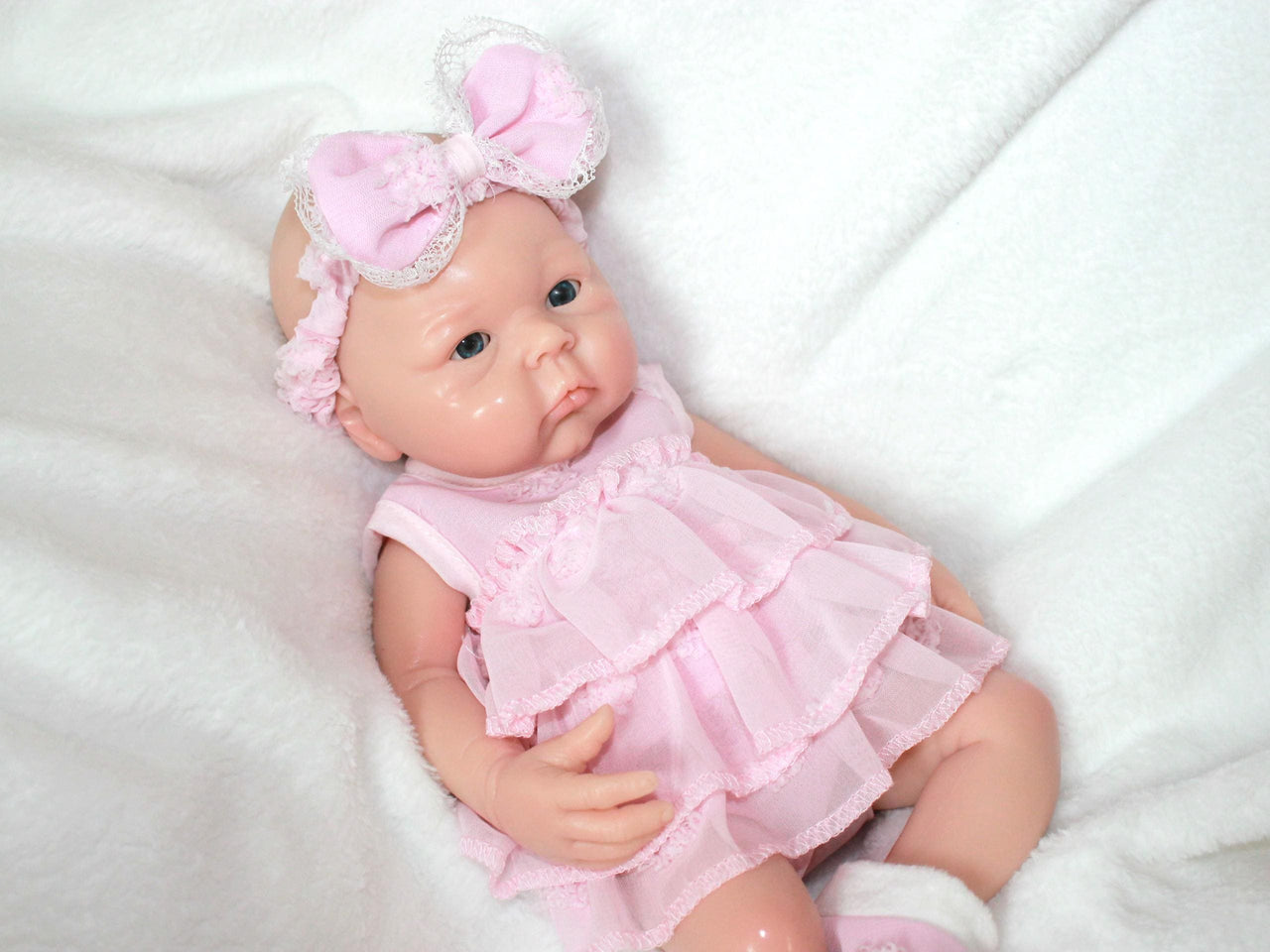 A baby doll dressed in a pink dress and matching headband, sitting against a soft background.