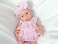 Thumbnail for A baby doll dressed in a pink dress and matching headband, sitting against a soft background.