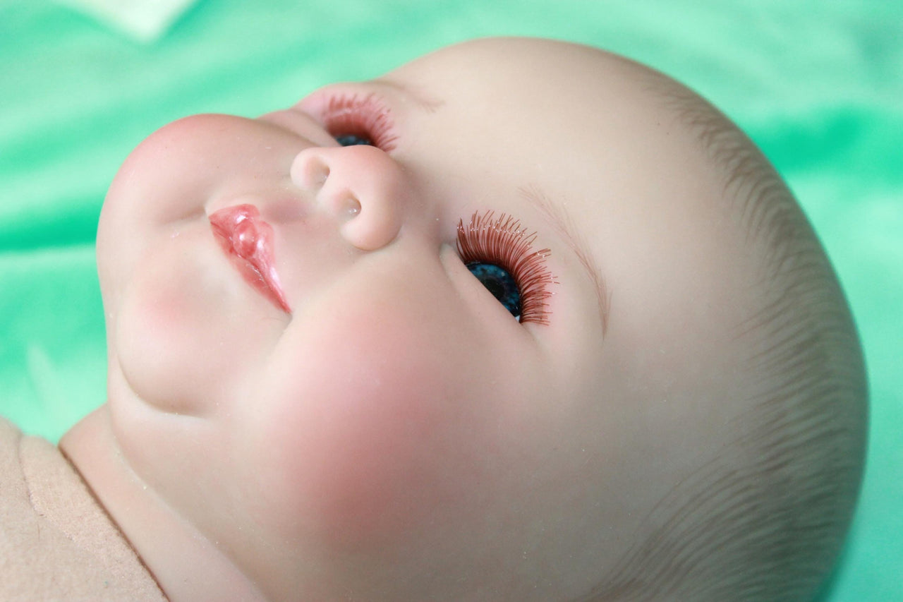 A baby doll positioned on a clean green sheet, highlighting its charming design and soft textures.