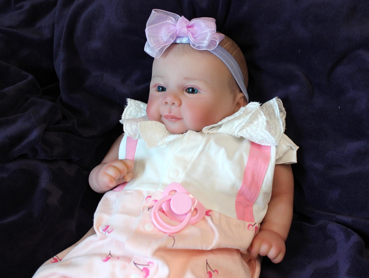 A baby doll positioned on a clean purple sheet, highlighting its charming design and soft textures.