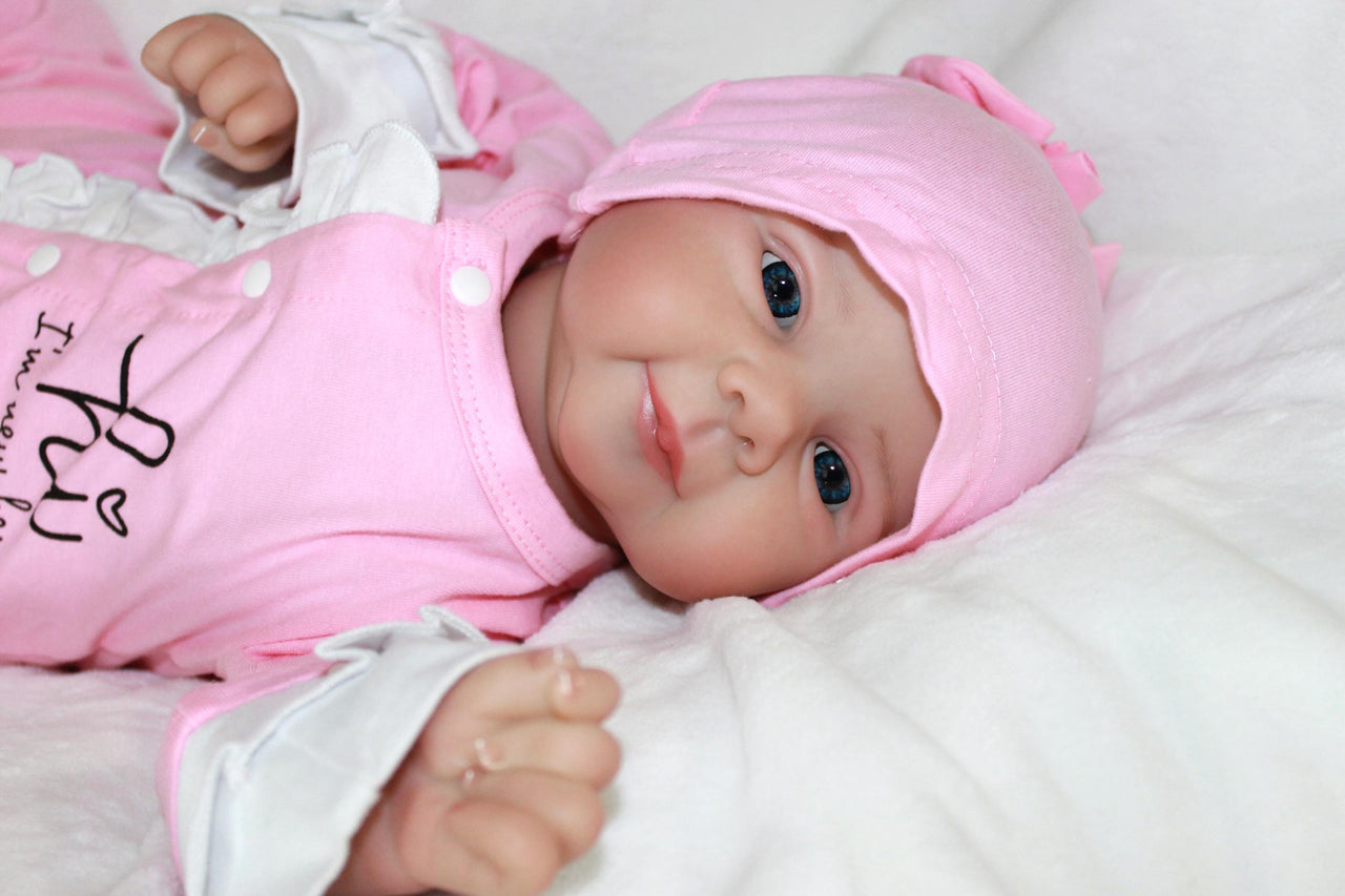 A baby doll resting on a purple sheet, showcasing its soft features and delicate clothing.