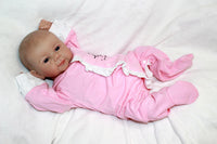Thumbnail for A baby doll resting on a purple sheet, showcasing its soft features and delicate clothing.
