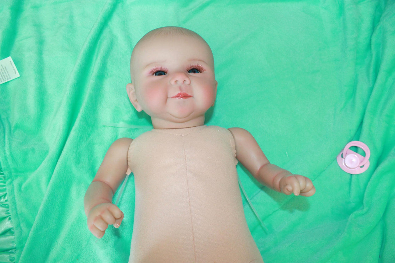 A baby doll resting on a green sheet, showcasing its soft features and delicate clothing.