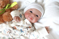 Thumbnail for A baby doll positioned on a clean green sheet, highlighting its charming design and soft textures.