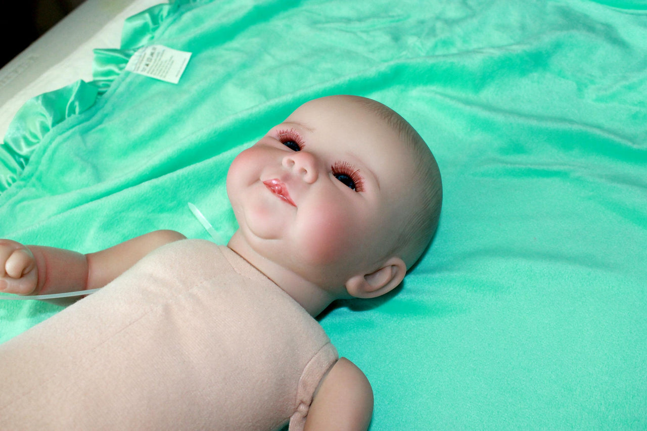 A baby doll positioned on a clean green sheet, highlighting its charming design and soft textures.