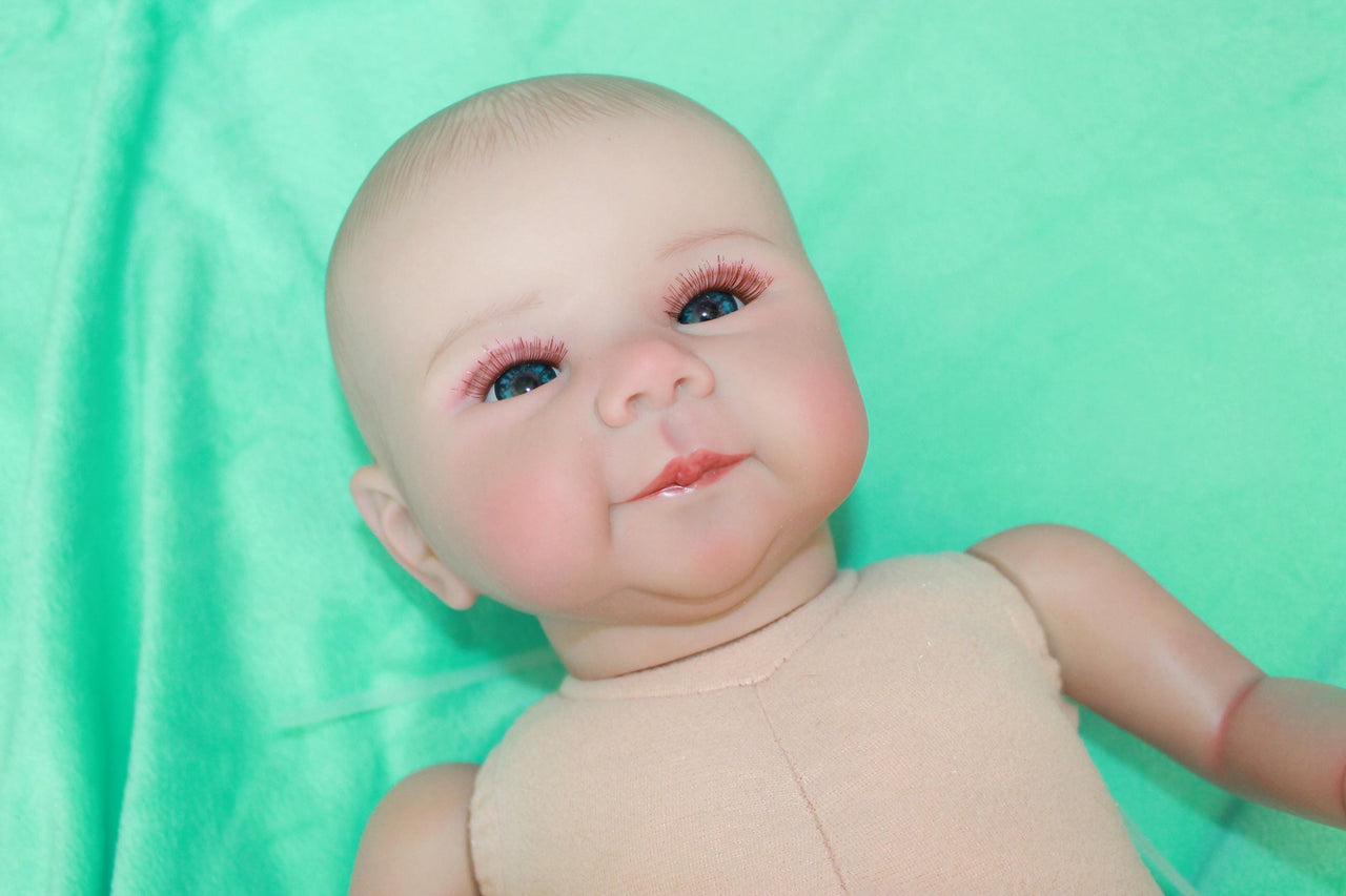 A baby doll lying on a pristine green sheet, emphasizing its adorable appearance and gentle colors.
