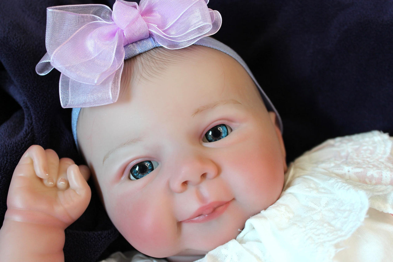 A baby doll positioned on a clean purple sheet, highlighting its charming design and soft textures.