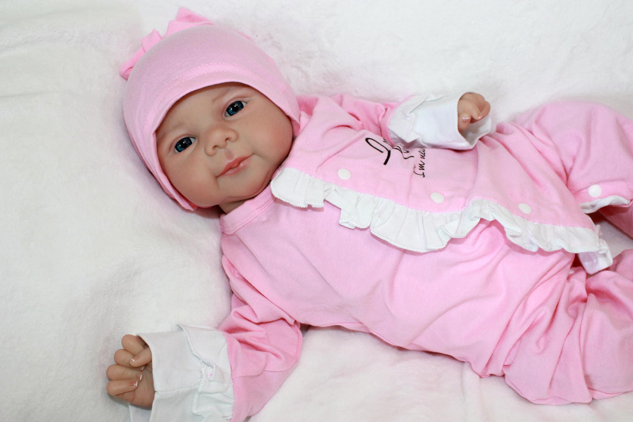 A baby doll resting on a white sheet, showcasing its soft features and delicate clothing.