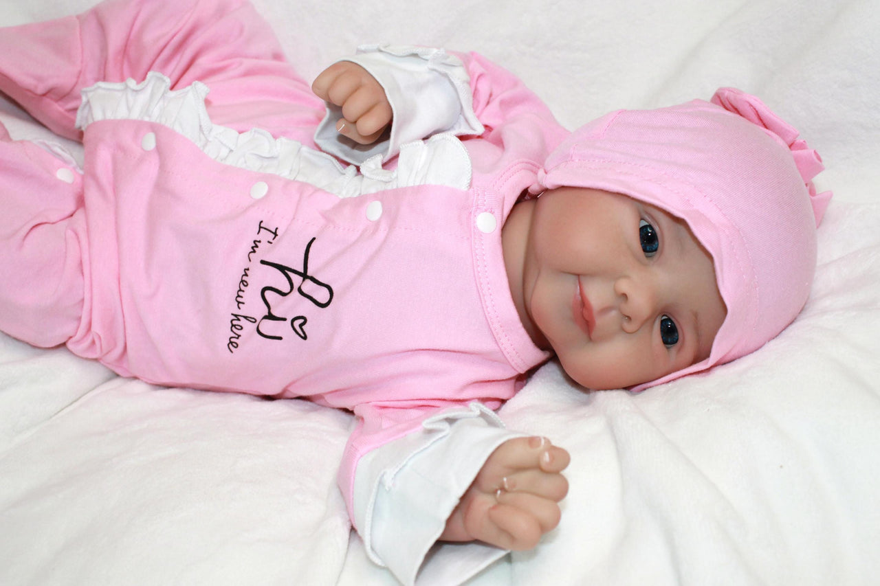 A baby doll resting on a purple sheet, showcasing its soft features and delicate clothing.