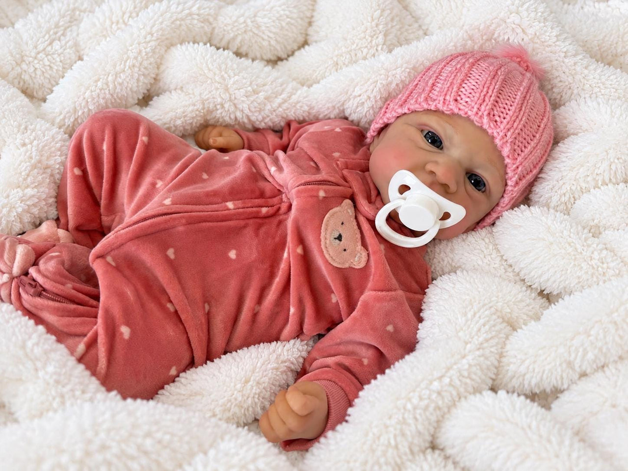 A baby doll with a pacifier lies on a cozy blanket, highlighting its charming design and soothing presence.