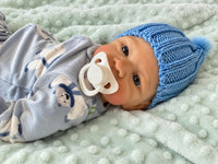 Thumbnail for A baby doll with a pacifier lies on a cozy blanket, highlighting its charming design and soothing presence.
