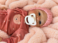 Thumbnail for A baby doll with a pacifier lies on a cozy blanket, highlighting its charming design and soothing presence.