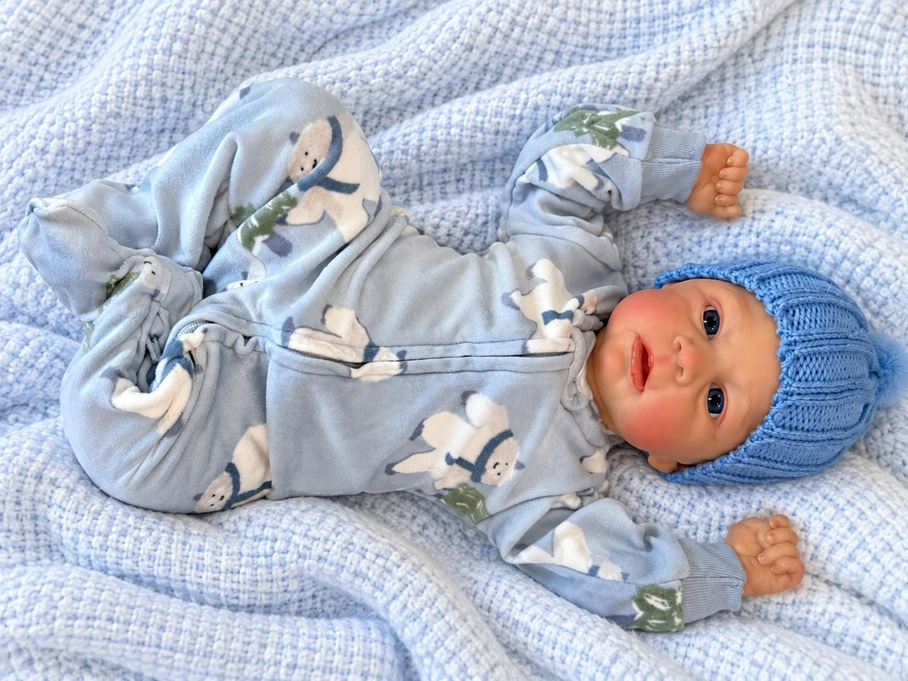 Realistic reborn baby doll featuring lifelike newborn details, delicate facial features, realistic skin texture, hand-painted details, and beautiful expressive eyes. Photographed resting naturally on a soft, cozy baby blanket to showcase the doll's realistic appearance and craftsmanship.