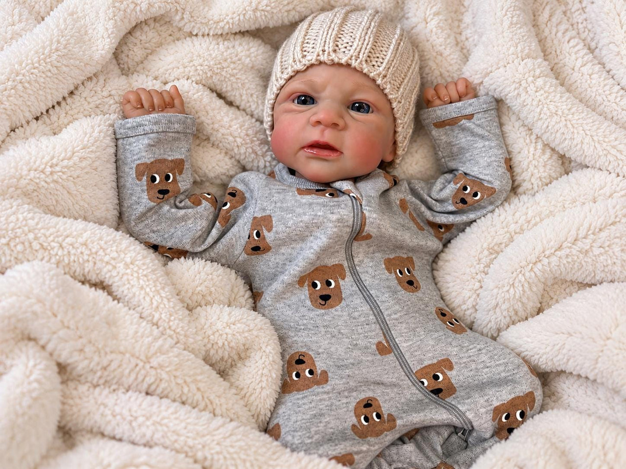 Realistic reborn baby doll featuring lifelike newborn details, delicate facial features, realistic skin texture, hand-painted details, and beautiful expressive eyes. Photographed resting naturally on a soft, cozy baby blanket to showcase the doll's realistic appearance and craftsmanship.