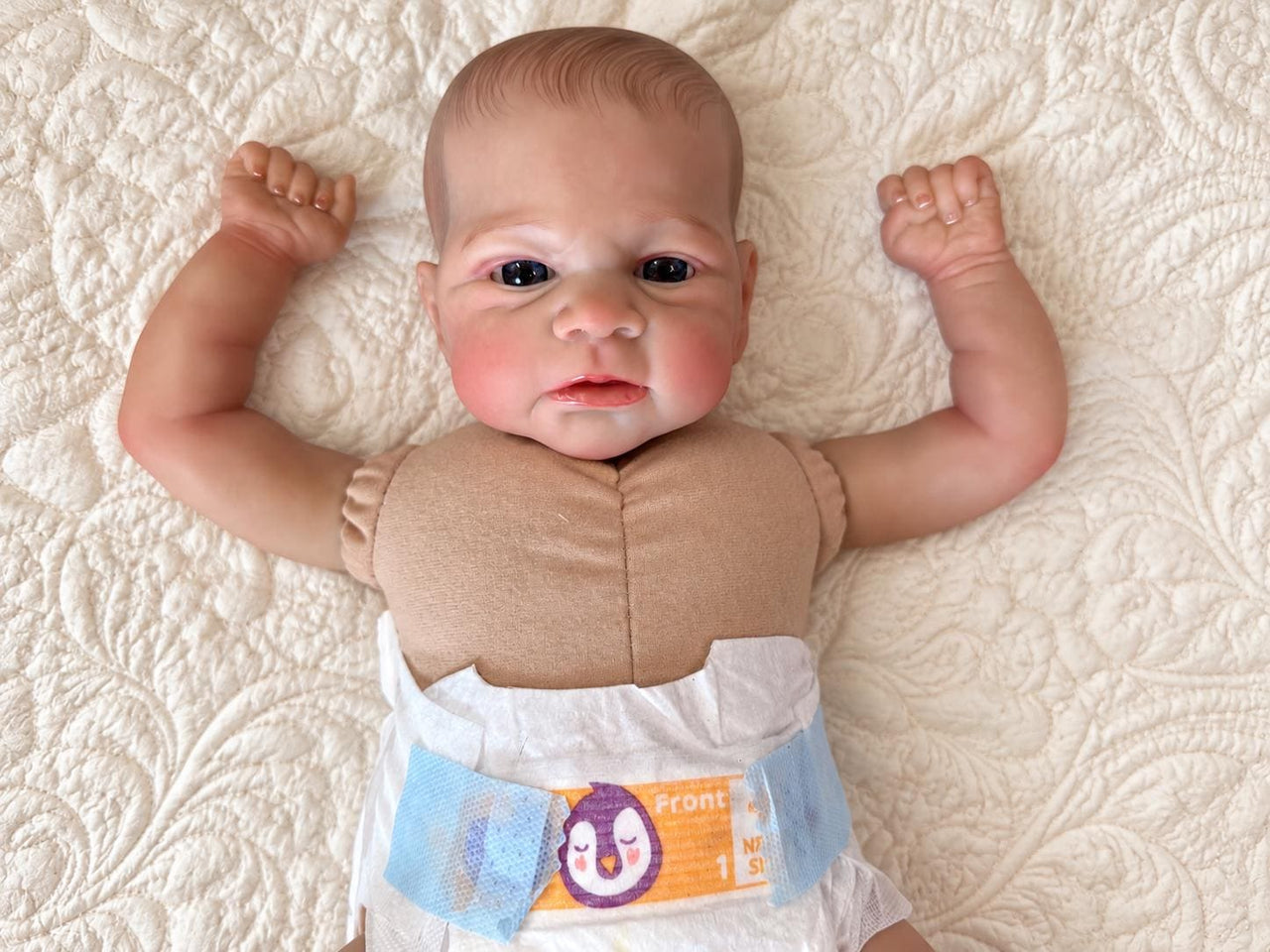 Realistic reborn baby doll featuring lifelike newborn details, delicate facial features, realistic skin texture, hand-painted details, and beautiful expressive eyes. Photographed resting naturally on a soft, cozy baby blanket to showcase the doll's realistic appearance and craftsmanship.